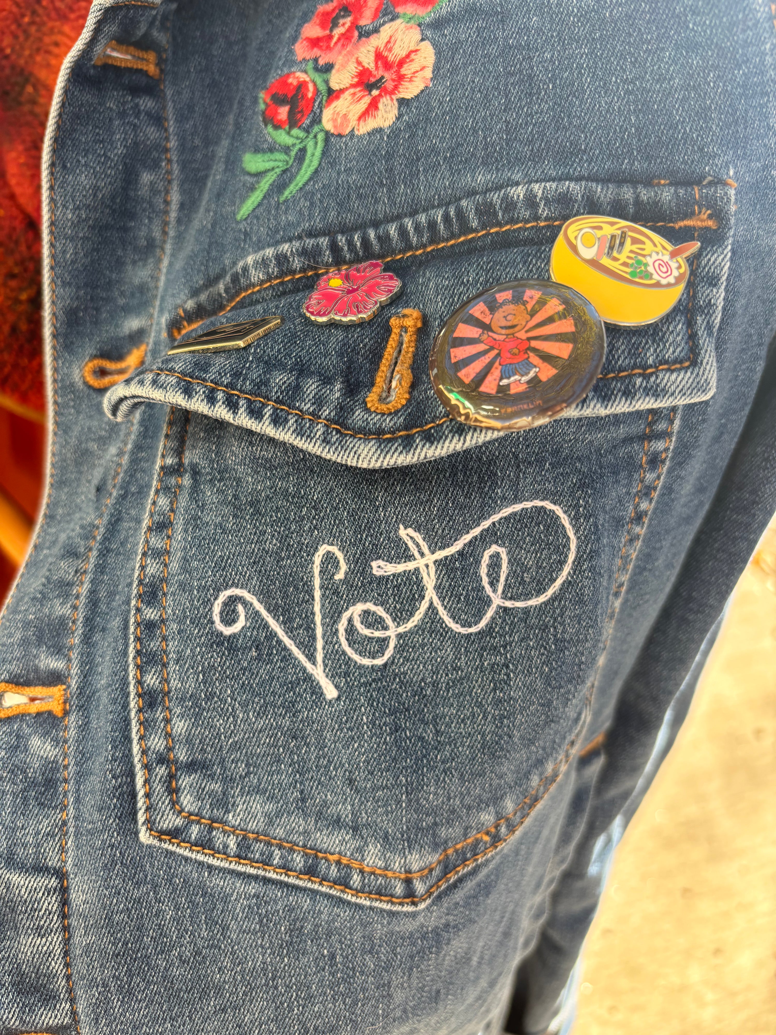 Custom chainstitch embroidered script embroidery of "Vote" on a denim jacket pocket.