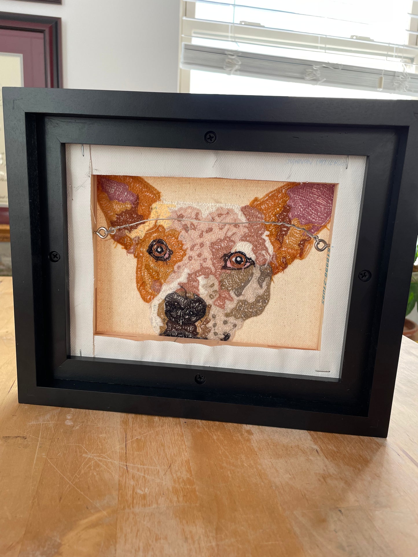 framed custom pet portrait chainstitch embroidered commission of a red cattle dog on a white canvas framed in a black frame - this is the rear view