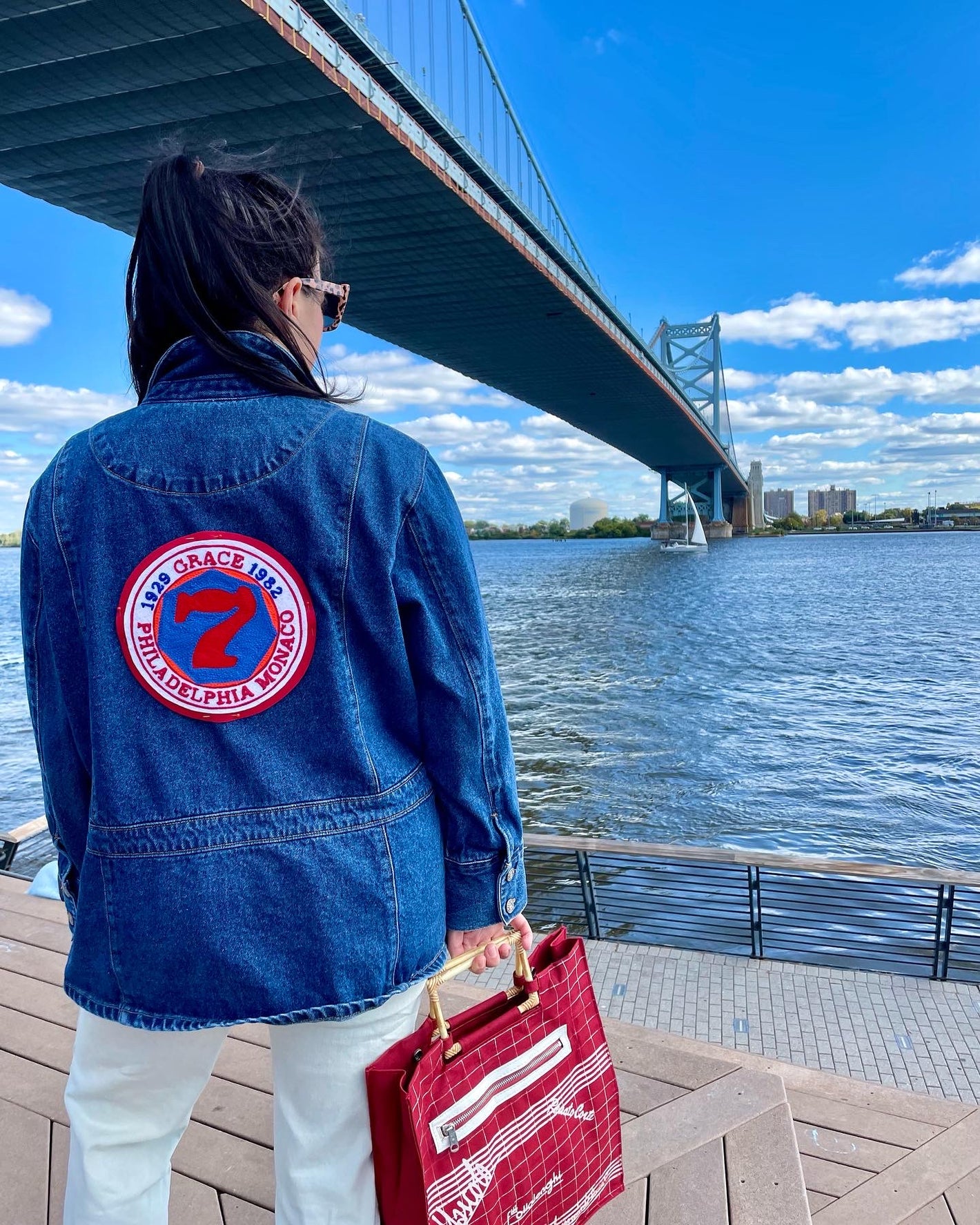 woman standing on a pier in a denim jacket with a custom chainstitched circular patch.  The patch has the number 7 on it with text embroidered around it in a circle 