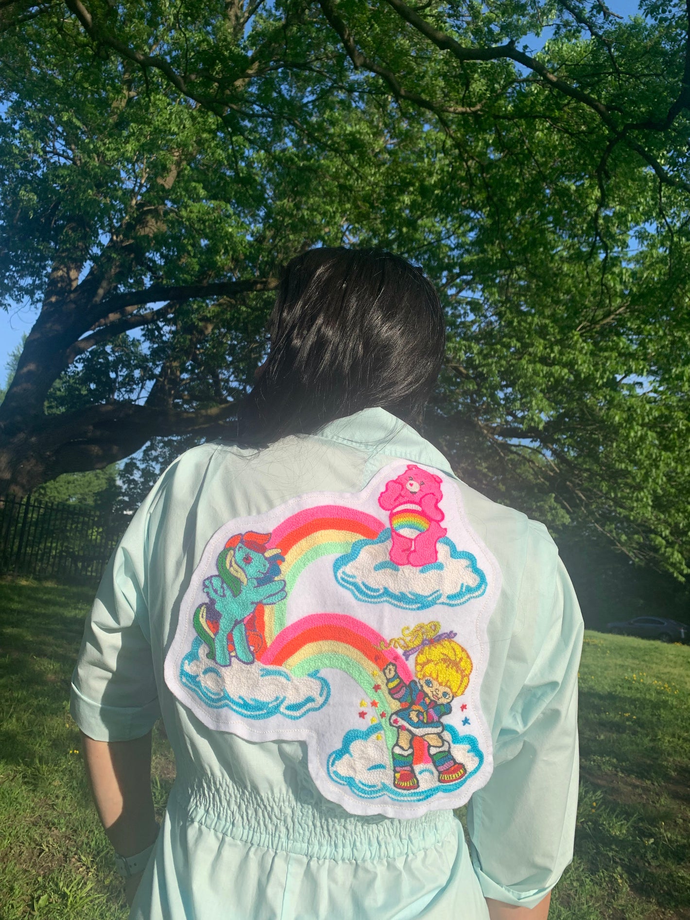 woman wearing a jumpsuit chainstitched with 80s cartoons featuring a care bear, a my little pony, and a rainbow brite photographed at Lemon Hill, Philadelphia.